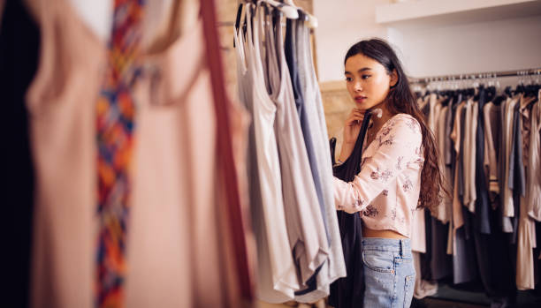 Asian hipster woman shopping for clothes inside a clothing store Beautiful young asian woman browsing and looking to buy summer clothes in a women's boutique summers clothes stock pictures, royalty-free photos & images