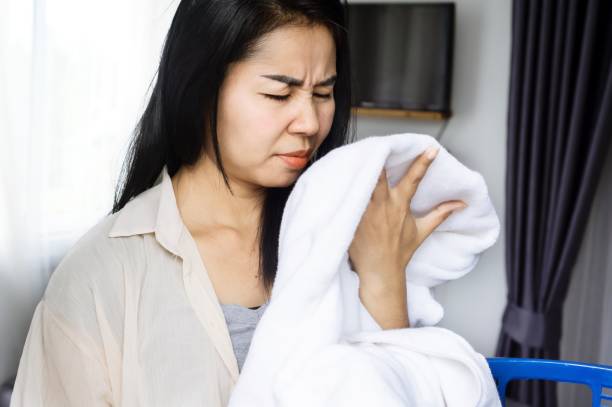 Asian housewife smelling stinky towel, woman having a problem with bad smell from clothes stock photo