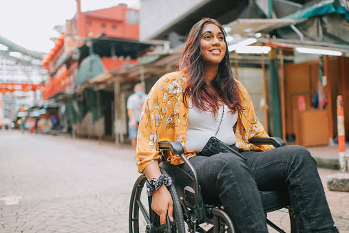 asian indian beautiful woman with disability using wheelchair exploring downtown district in kuala lumpur