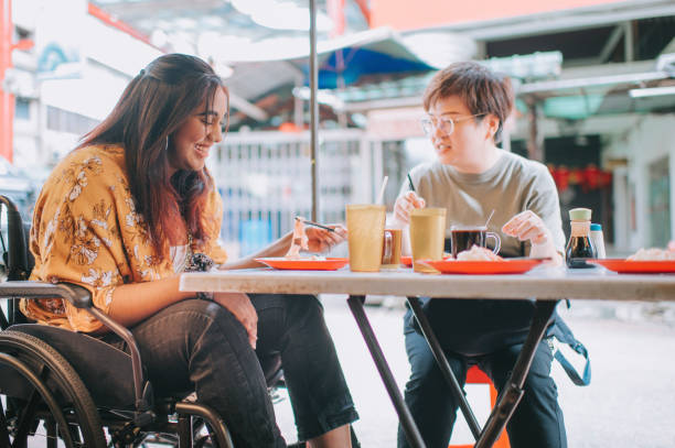 asian indian woman with disability on wheelchair enjoying street food in petaling street with her chinese female friend - wheelchair street happy imagens e fotografias de stock