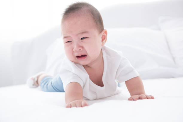 Asian infant crying baby. child tired and hungry on white bed stock photo