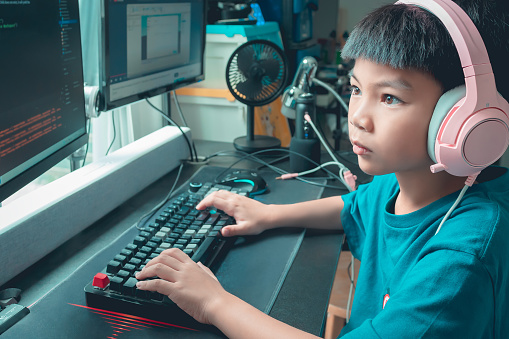 Asian kid is coding and scripting program on on his game streaming desktop computer with headphone on.