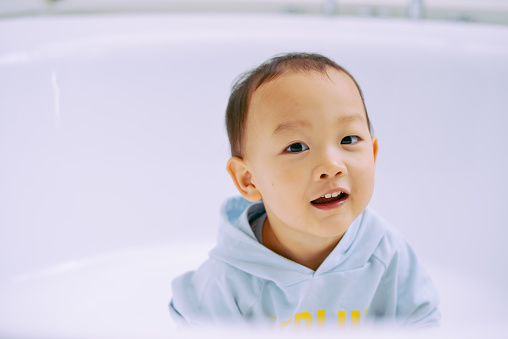 One cute Asian kid looking at camera curiously in bathtub