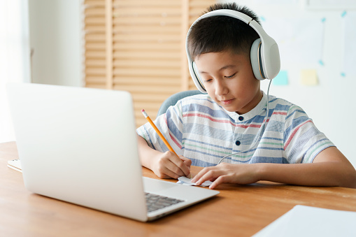 Asian little boy video call online via the internet tutor on a computer laptop with headphones. Asia man doing homework. Concept online learning at home