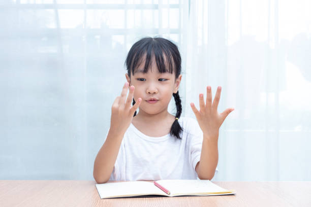 Asian little Chinese Girl doing mathematics by counting fingers stock photo