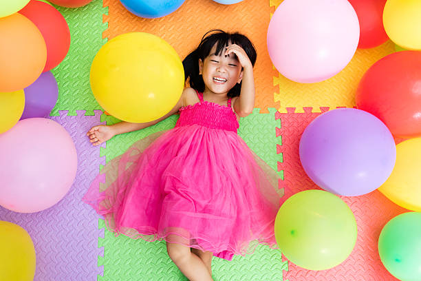 Asian Little Chinese Girl Lying on Floor amongst Balloons stock photo