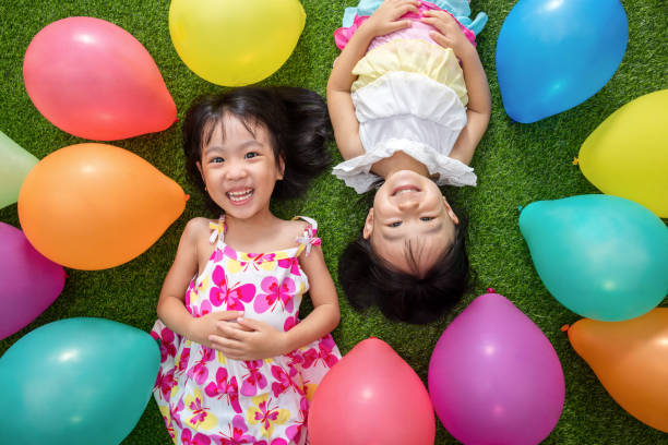 Asian little Chinese girls lying on grass amongst colorful balloons stock photo