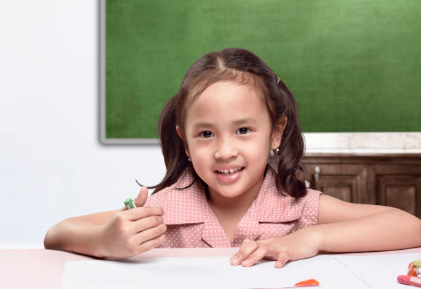 Asian little girl with a crayon drawing in the paper on the table Asian little girl with a crayon drawing in the paper on the table. Back to School concept philippines girl stock pictures, royalty-free photos & images