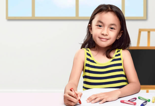 Asian little girl with a crayon drawing in the paper on the table Asian little girl with a crayon drawing in the paper on the table. Back to School concept indonesian girl stock pictures, royalty-free photos & images