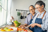 istock Asian loving senior elderly couple wear apron and cooking in kitchen. Attractive strong old man and woman grandparent wear eyeglass enjoy retirement life activity at home. Family relationship concept. 1362493500