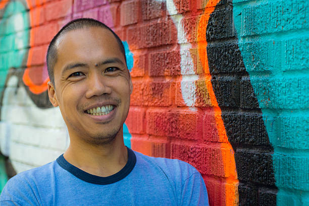 Asian male standing against graffiti wall, smiling stock photo