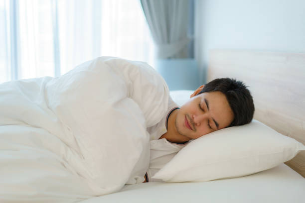 Asian man are sleeping and having good dreams in white blanket in the morning. Rest after work tiring in bedroom at home stock photo