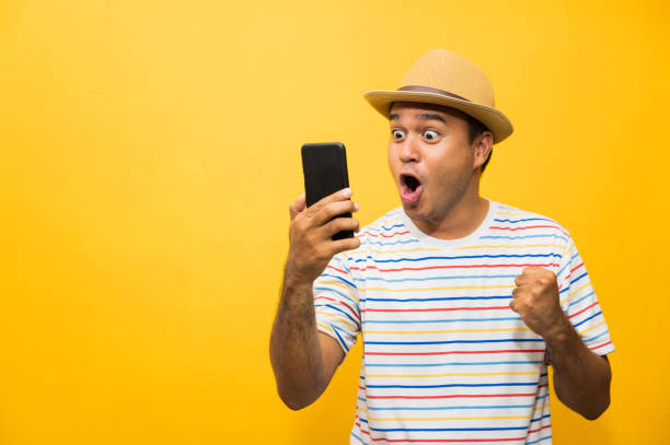 Asian man happy with his smartphone on yellow background. young man using looking at smartphone. stock photo