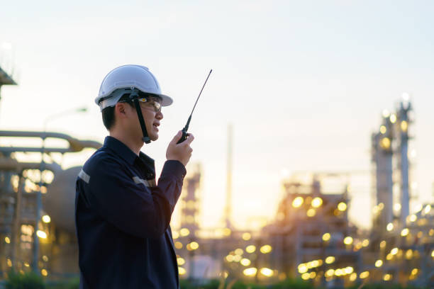 Asian man technician Industrial engineer using walkie-talkie and holding bluprint working in oil refinery for building site survey in civil engineering project. stock photo