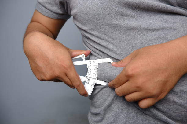 asian man wearing grey shirt checking his fat belly with calipers asian man wearing grey shirt checking his fat belly with calipers obesity stock pictures, royalty-free photos & images
