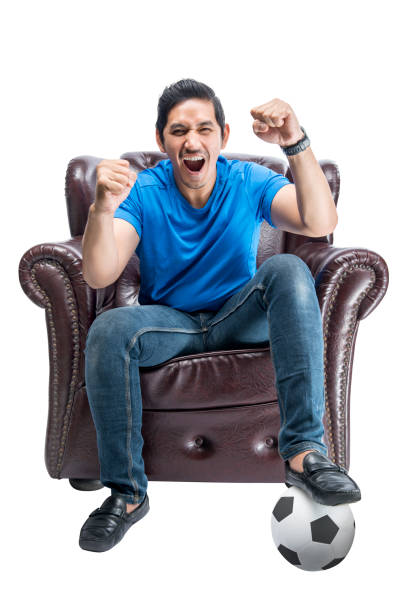 Asian man with the ball sitting on the couch with an excited expression stock photo