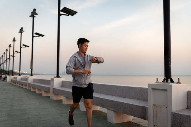 Asian men look at smartwatches to check their heartbeat while jogging in a beach park. stock photo