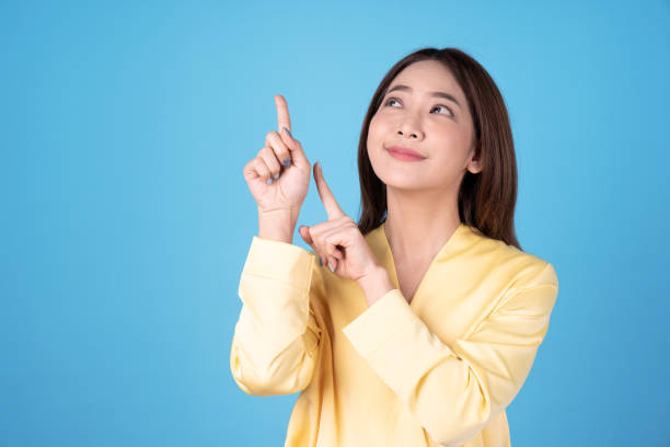 Asian model pointing fingers at an empty space next to her, Isolated on a blue background. stock photo