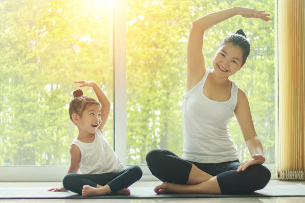 asian mom practice yoga at home with a adorable daughter sitting next to her, trying to imitate the mother's posture with a smiling face while exercise at home. - yoga crianças imagens e fotografias de stock