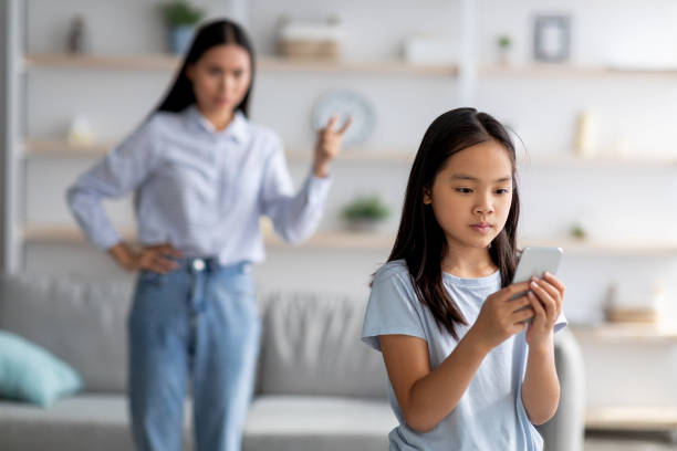 アジアの母と娘は、スマートフォンを使い過ぎるために喧嘩し、女の子は彼女のお母さんに注意を払っていない - 子ども　言い争い ストックフォトと画像