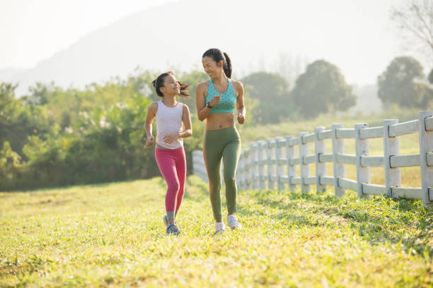 Asian mother and daughter run in forest park stock photo