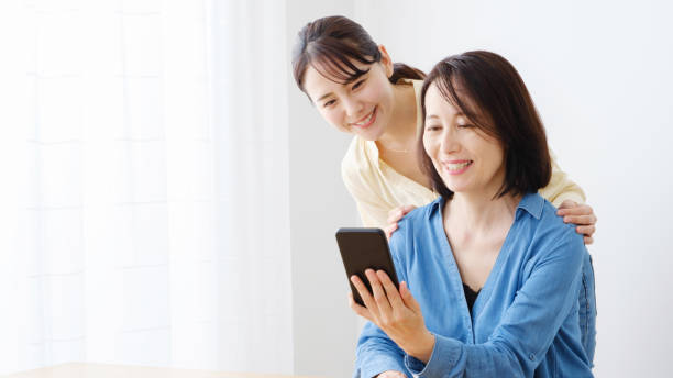 リビングルームでスマートフォンを使用してアジアの母と娘 - スマホ　女性　日本人 ストックフォトと画像