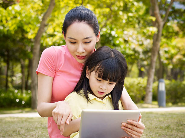 asian mother and daughter using tablet computer asian mother and daughter using tablet computer outdoors. child korea little girls korean ethnicity stock pictures, royalty-free photos & images
