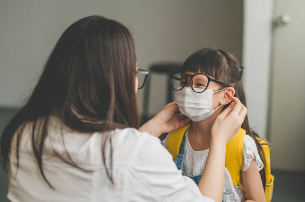 Asian mother help her daughter wearing face mask for protection Coronavirus outbreak Image of Asian mother help her daughter wearing medical mask to prepare go to school. Avoiding Covid-19 or coronavirus outbreak. back to school stock pictures, royalty-free photos & images