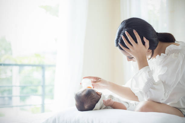 doğum sonrası depresyon muzdarip yatakta yenidoğan bebek için formül sütü asya anne kreş besleme şişesi. sağlık tek anne annelik stresli kavramı. - baby formula stok fotoğraflar ve resimler