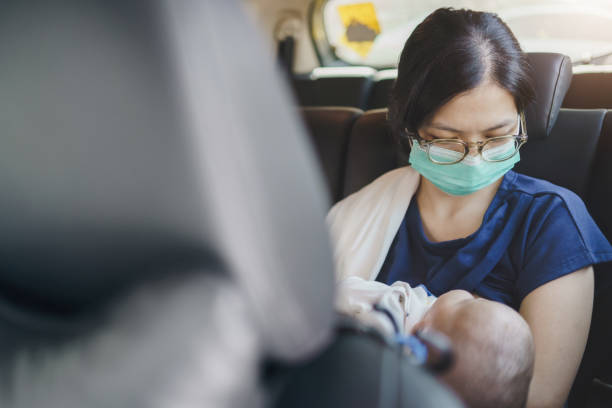 Asian Mother wearing Protective face mask holding newborn baby boy and breastfeeding while sitting inside car stock photo