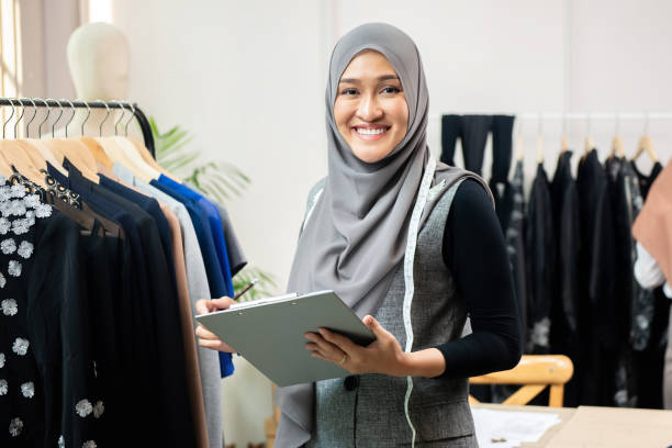 Asian muslim woman designer in her tailor shop Happy smiling Asian muslim woman designer as a startup business owner working in her tailor shop indonesian woman stock pictures, royalty-free photos & images