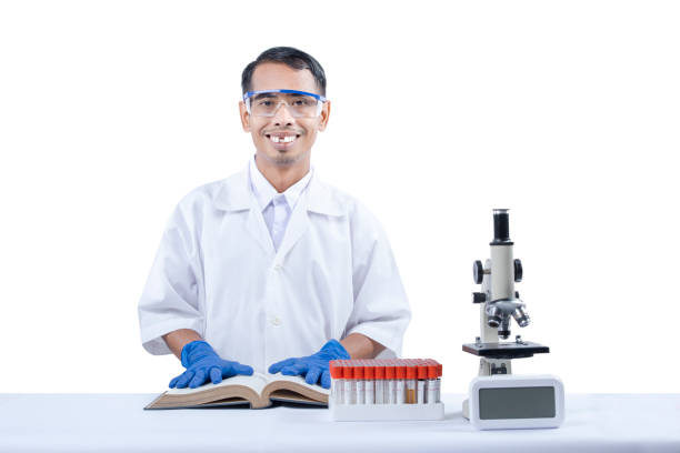 Asian nerd scientist standing and holding a book with a microscope and medical tube rack on the desk stock photo