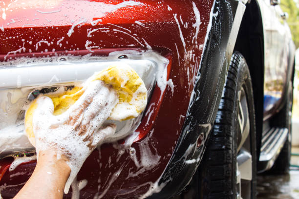 asiatische alter mann mit gelben schwamm waschen vorne nebelscheinwerfer neue rote autos. hintergrund mit textfreiraum reinigung. - waschen stock-fotos und bilder