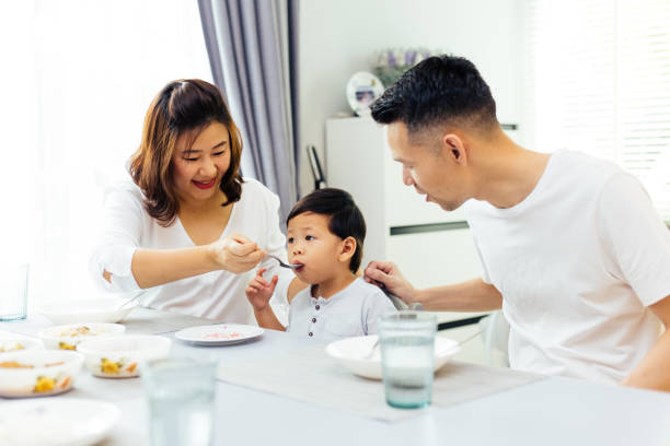Asian parents feeding their child and the whole family having meal together at home Asian parents feeding their child and the whole family having meal together at home asian family eating together stock pictures, royalty-free photos & images