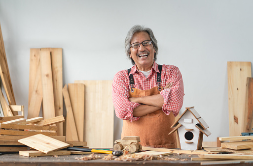 Asian senior carpenter man with crossed arms smile at home carpentry workshop