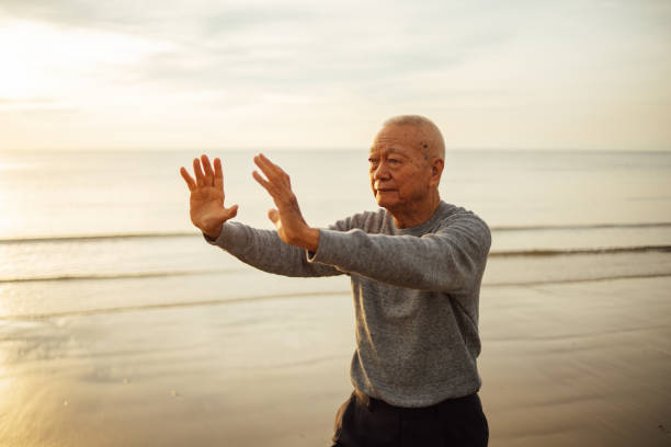 Asian Senior old man practice Tai chi and Yoga pose on the beach sunrise stock photo