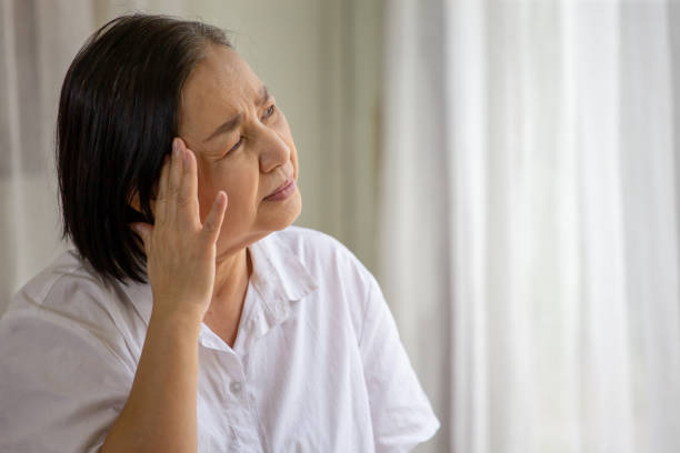 Asian senior woman sitting on sofa having headache at home. old female   stressed dizzy . elderly touching her head with her hands while having migraine or alzheimer .memory loss . indoor. copy space stock photo