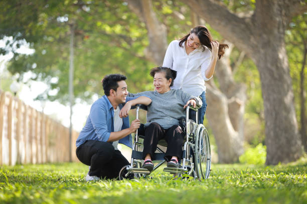 Asian senior woman sitting on the wheelchair with family happy smile face on the green park stock photo