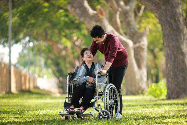 Asian senior woman sitting on the wheelchair with her son  happy smile face on the green park stock photo