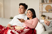 クリスマスイブを楽しむアジアの配偶者がリビングルームでテレビを見ている
