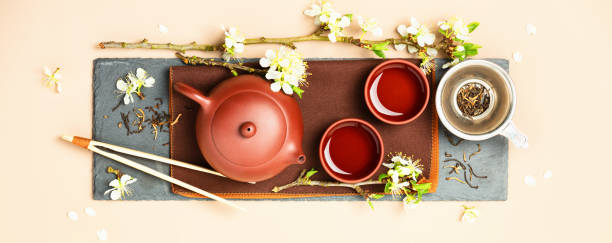 Asian Tea set on stone slate board, ceramic teapot, cups, dried tea and spring branches stock photo