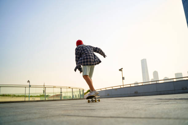 asian teenage boy skateboarding outdoors stock photo