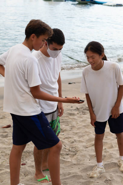 aziatische tieners met mobiel apparaat op het strand dat pret heeft die spelen spelletjes speelt - beach game group stockfoto's en -beelden