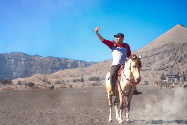 азиатский путешественник использовать смартфон селфи между ездить на лошади - semeru стоковые фото и изображения