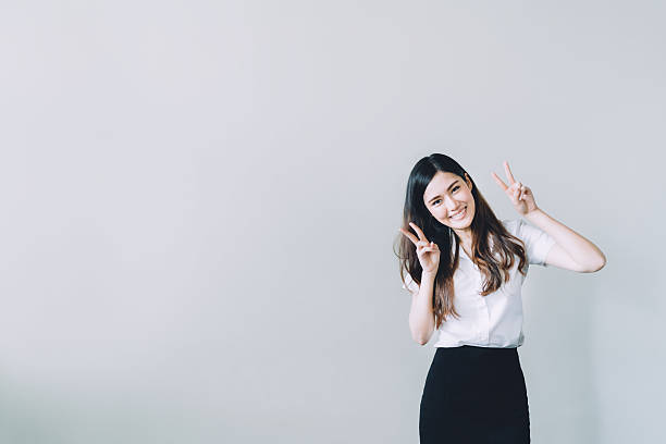 Asian university girl doing funny rabbit pose, with copy space Cute asian university girl doing funny rabbit pose, copy space on gray wall background cute thai girl stock pictures, royalty-free photos & images