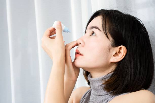 Asian woman applying eye drops to refresh from dry, tired eyes stock photo