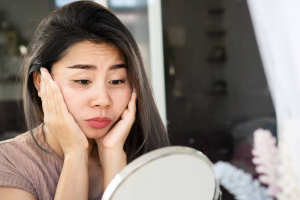 Asian woman checking her eyes bags , dark circles, wrinkle and crow's feet on her face skin with a mirror stock photo