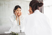 アジアの女性は、ミラー、スキンケアと化粧品除去コンセプトの顔の前面をクリーニング