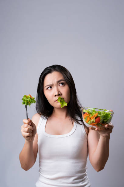 Asian woman confused with eating salad isolated over white background. stock photo