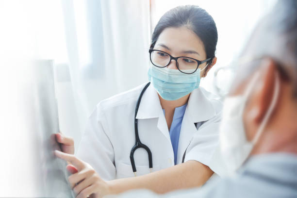Asian woman Doctor in surgical mask giving advice to old man patient Physician talking with senior man at clinic pandemic during Covid-19 or Coronavirus. Asian woman Doctor wear eyeglasses and surgical mask giving advice to Elderly patient in medical room at hospital physician stock pictures, royalty-free photos & images